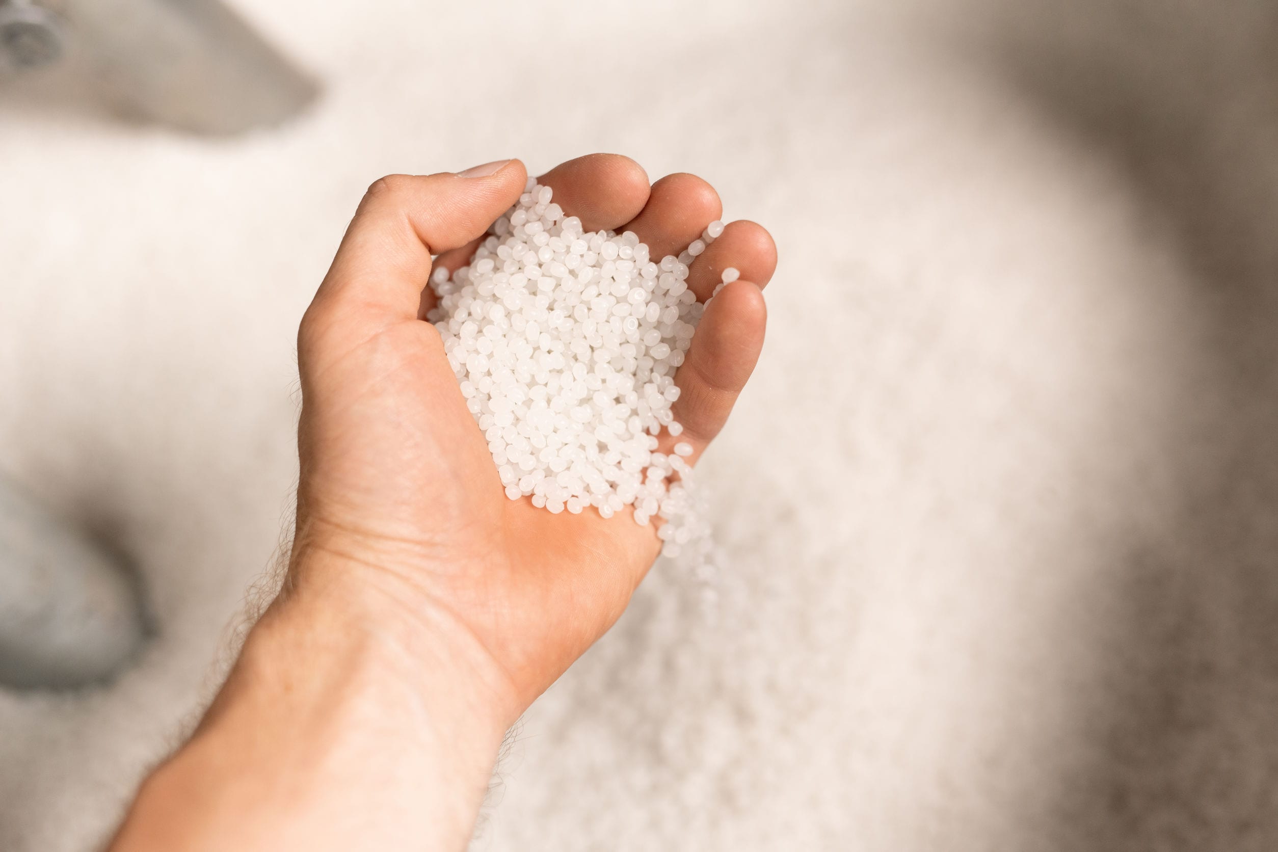 Hand of young male worker of large modern factory holding polymer granules